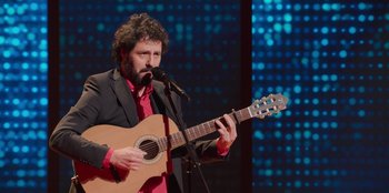 Movie still from “All About Gila” (2022), directed by Arturo González-Campos – A man with a beard is holding a guitar; Medium shot, Low angle