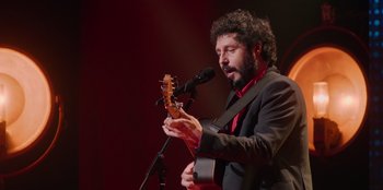 Movie still from “All About Gila” (2022), directed by Arturo González-Campos – A man in a suit playing an instrument on a stage; Medium shot, Low angle