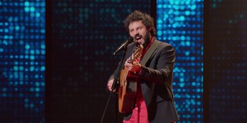 Movie still from “All About Gila” (2022), directed by Arturo González-Campos – A man with a beard is playing an instrument; Medium shot, Low angle