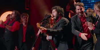 Movie still from “All About Gila” (2022), directed by Arturo González-Campos – A man and woman sing together while holding a guitar; Medium shot, Low angle