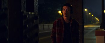 Movie still from “All the Bright Places” (2020), directed by Brett Haley – A young man wearing headphones standing on the side of the road; Medium shot, Over the shoulder angle