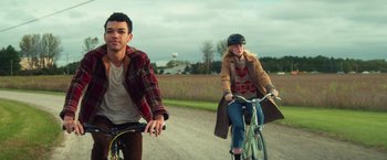 Movie still from “All the Bright Places” (2020), directed by Brett Haley – A man and a woman riding bikes down a dirt road; Medium shot, Over the shoulder angle