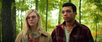 Movie still from “All the Bright Places” (2020), directed by Brett Haley – A man and a woman standing next to each other in front of trees; Medium shot, Low angle