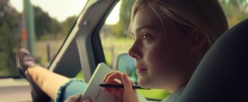 Movie still from “All the Bright Places” (2020), directed by Brett Haley – A woman sitting in the back of a car writing on a notebook; Close Up shot, Over the shoulder angle