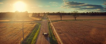 Movie still from “All the Bright Places” (2020), directed by Brett Haley – A truck driving down a road near a field of brown grass; Extreme Wide shot, High angle