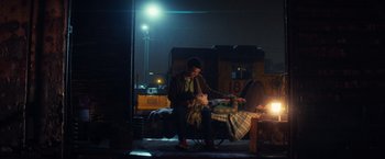Movie still from “All the Bright Places” (2020), directed by Brett Haley – A man sitting on a bench next to a fire hydrant at night; Wide shot, High angle