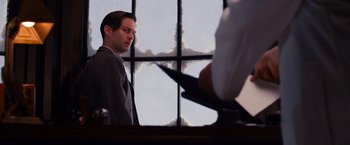 Movie still from “The Great Gatsby” (2013), directed by Baz Luhrmann – A man standing in front of a window with a computer; Medium shot, Over the shoulder angle