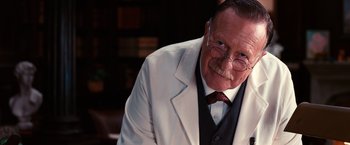 Movie still from “The Great Gatsby” (2013), directed by Baz Luhrmann – An older man wearing glasses and a white jacket; Close Up shot, Low angle