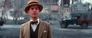 Movie still from “The Great Gatsby” (2013), directed by Baz Luhrmann – A man wearing a suit and a bow tie standing in the middle of a street; Close Up shot, Low angle