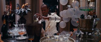 Movie still from “The Great Gatsby” (2013), directed by Baz Luhrmann – A man pouring a drink into a wine glass at a party; Medium shot, High angle