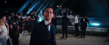 Movie still from “The Great Gatsby” (2013), directed by Baz Luhrmann – A man in a suit and bow tie standing in front of a crowd; Medium shot, Over the shoulder angle