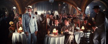 Movie still from “The Great Gatsby” (2013), directed by Baz Luhrmann – A group of people sitting around a table with a cake; Wide shot, Over the shoulder angle