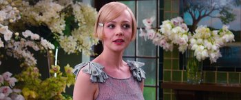 Movie still from “The Great Gatsby” (2013), directed by Baz Luhrmann – A woman in a pink and gray dress with flowers in the background; Close Up shot, Over the shoulder angle