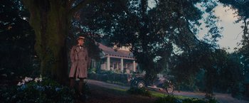 Movie still from “The Great Gatsby” (2013), directed by Baz Luhrmann – A man standing in front of a house with a car parked in front of it; Wide shot, Low angle