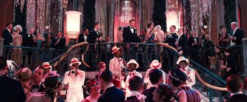 Movie still from “The Great Gatsby” (2013), directed by Baz Luhrmann – A group of people standing in a room with hats on; Wide shot, High angle