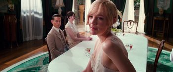 Movie still from “The Great Gatsby” (2013), directed by Baz Luhrmann – A woman sitting in front of two other people at a table; Medium shot, Over the shoulder angle