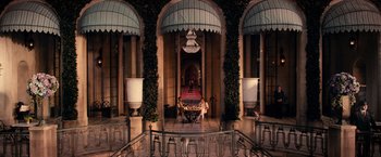 Movie still from “The Great Gatsby” (2013), directed by Baz Luhrmann – Two people sitting at a table in front of an entrance to a building; Extreme Wide shot, High angle