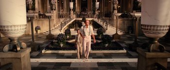 Movie still from “The Great Gatsby” (2013), directed by Baz Luhrmann – A man and a woman are standing in front of a building; Wide shot, Low angle