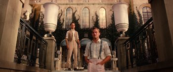 Movie still from “The Great Gatsby” (2013), directed by Baz Luhrmann – A couple of men standing next to each other on steps; Wide shot, Low angle