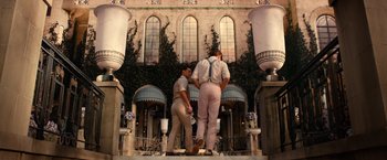 Movie still from “The Great Gatsby” (2013), directed by Baz Luhrmann – A couple of men standing on top of a staircase; Wide shot, Low angle