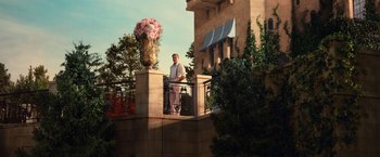 Movie still from “The Great Gatsby” (2013), directed by Baz Luhrmann – A man standing on a balcony next to a flower pot; Wide shot, Low angle