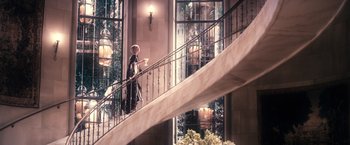 Movie still from “The Great Gatsby” (2013), directed by Baz Luhrmann – A woman walking down a staircase holding a cup of coffee; Wide shot, High angle
