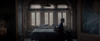 Movie still from “All the Old Knives” (2022), directed by Janus Metz – A man sitting on top of a bed next to a window; Wide shot, High angle