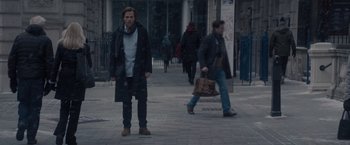 Movie still from “All the Old Knives” (2022), directed by Janus Metz – A man is standing on the sidewalk in the rain; Wide shot, Over the shoulder angle