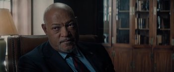 Movie still from “All the Old Knives” (2022), directed by Janus Metz – A man in a suit and tie sitting in front of a bookshelf; Close Up shot, Over the shoulder angle