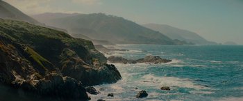 Movie still from “All the Old Knives” (2022), directed by Janus Metz – A body of water near a mountain range with waves crashing on it's shore; Extreme Wide shot, High angle