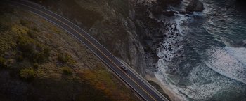 Movie still from “All the Old Knives” (2022), directed by Janus Metz – An aerial view of a car driving on a road near the ocean; Extreme Wide shot, High angle
