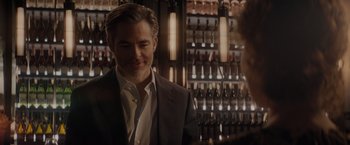 Movie still from “All the Old Knives” (2022), directed by Janus Metz – A man in a suit and tie in front of bottles; Medium shot, Over the shoulder angle