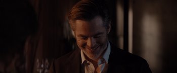 Movie still from “All the Old Knives” (2022), directed by Janus Metz – A person wearing a suit and smiling; Close Up shot, Over the shoulder angle
