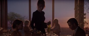 Movie still from “All the Old Knives” (2022), directed by Janus Metz – A woman standing at a dinner table with a bottle of wine; Medium shot, Over the shoulder angle