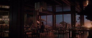 Movie still from “All the Old Knives” (2022), directed by Janus Metz – People are sitting at tables in a restaurant with large windows; Wide shot, Low angle