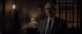 Movie still from “All the Old Knives” (2022), directed by Janus Metz – An older man wearing a suit and tie in front of a lamp; Close Up shot, Over the shoulder angle