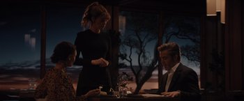 Movie still from “All the Old Knives” (2022), directed by Janus Metz – A group of people sitting at a table with food and wine; Medium shot, Over the shoulder angle