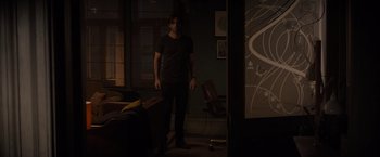 Movie still from “All the Old Knives” (2022), directed by Janus Metz – A man standing in a dark room in front of a projector screen; Wide shot, Over the shoulder angle