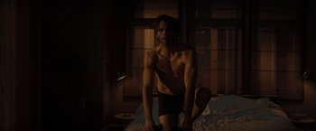 Movie still from “All the Old Knives” (2022), directed by Janus Metz – A shirtless man kneeling on a bed in the dark; Medium shot, Low angle