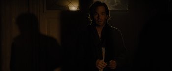 Movie still from “All the Old Knives” (2022), directed by Janus Metz – A man standing in a dark room holding a cell phone; Medium shot, Over the shoulder angle