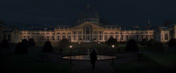 Movie still from “All the Old Knives” (2022), directed by Janus Metz – A person standing in front of a fountain in front of a building at night; Extreme Wide shot, Low angle