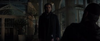 Movie still from “All the Old Knives” (2022), directed by Janus Metz – A man in a black coat standing next to a bottle of soda; Medium shot, Over the shoulder angle