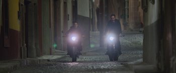 Movie still from “All the Places” (2023), directed by Pitipol Ybarra – Two people riding motorcycles down a street at night; Wide shot, Low angle