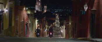 Movie still from “All the Places” (2023), directed by Pitipol Ybarra – Two people riding motorcycles down a street at night; Extreme Wide shot, Low angle