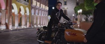 Movie still from “All the Places” (2023), directed by Pitipol Ybarra – A man riding a motorcycle down a street at night; Medium shot, Low angle