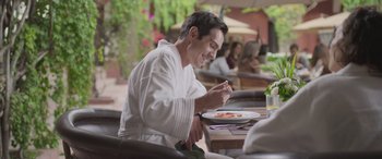 Movie still from “All the Places” (2023), directed by Pitipol Ybarra – A man sitting at a table with a plate in front of him; Medium shot, Over the shoulder angle