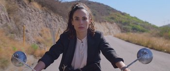 Movie still from “All the Places” (2023), directed by Pitipol Ybarra – A woman riding a motorcycle down a road; Close Up shot, High angle