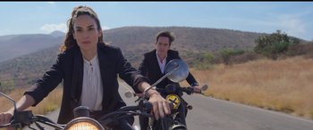 Movie still from “All the Places” (2023), directed by Pitipol Ybarra – A man and a woman riding a motorcycle down a road; Medium shot, Over the shoulder angle