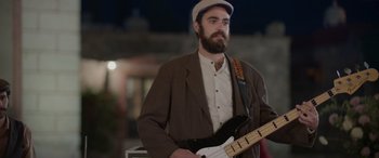 Movie still from “All the Places” (2023), directed by Pitipol Ybarra – A man with a beard holding a bass guitar; Medium shot, Low angle