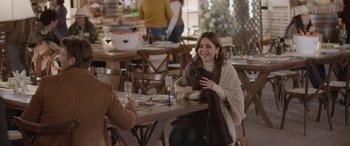 Movie still from “All the Places” (2023), directed by Pitipol Ybarra – A woman sitting at a table with a glass of wine; Medium shot, Over the shoulder angle